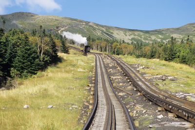 Mount washington railway cogwheel track on a sunny day with a steam locomotive in the background.