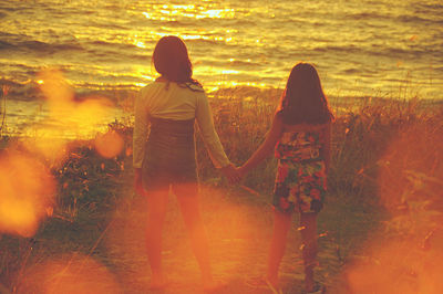 Rear view of siblings standing at beach during sunset