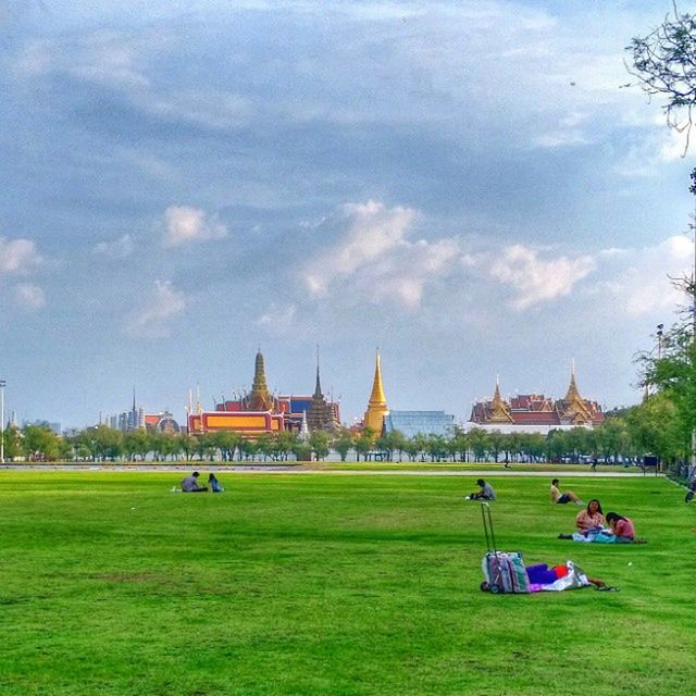 grass, sky, cloud - sky, lawn, architecture, built structure, tree, leisure activity, building exterior, person, lifestyles, large group of people, green color, men, tourism, cloud, park - man made space, travel, sitting