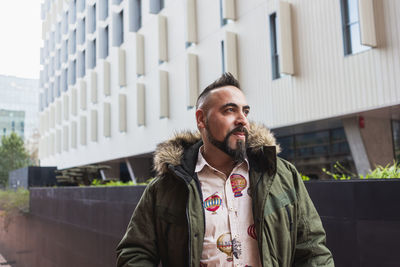 Bearded man standing and relaxing on stairs against office building