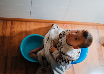 High angle view of cute baby boy with feet in bucket sitting at home