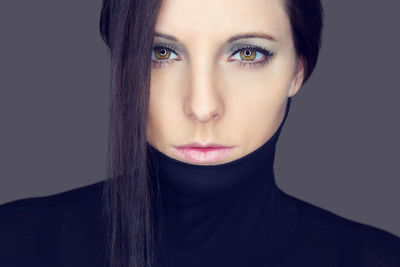 Close-up portrait of young woman wearing turtleneck against gray background