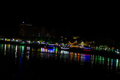 Illuminated city by river against sky at night