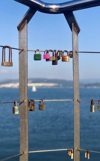 Padlocks on railing by sea against sky