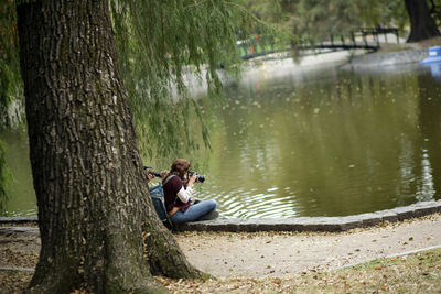 Man sitting on tree trunk by lake