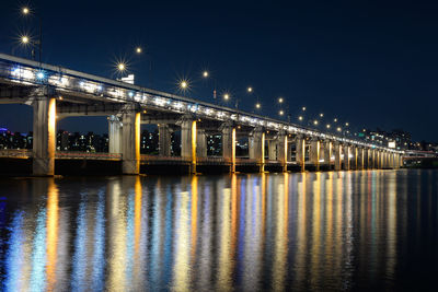 Illuminated bridge over river against sky at night