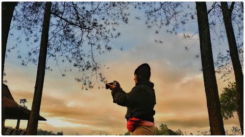 Side view of woman photographing against sky during sunset