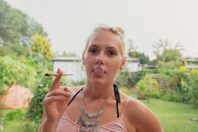 Portrait of young woman smoking marijuana joint while standing outdoors