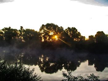 Trees by lake against sky during sunset
