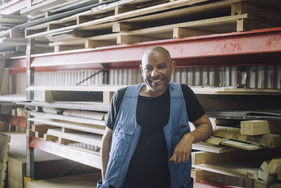 Portrait of smiling bald carpenter standing by pallet stack in warehouse