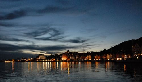 River by illuminated city against sky at sunset