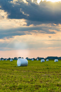 Hay bales on field against sky during sunset