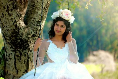 Portrait of smiling bride wearing wedding dress standing at park