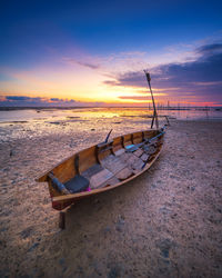 Boat moored on shore against sky during sunset