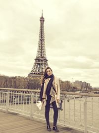 Portrait of woman standing by railing against eiffel tower