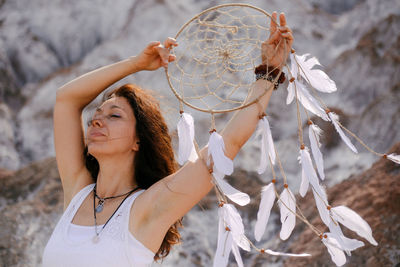 Woman's portrait with closed eyes. she is in white dress holding a dreamcatcher over her head.