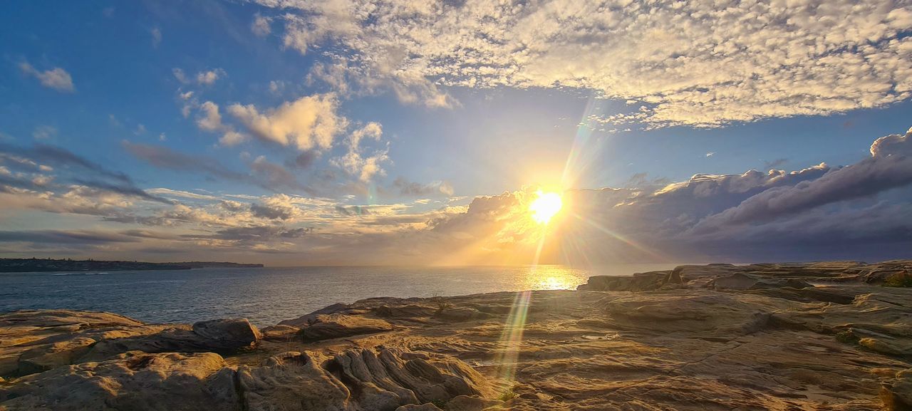 sky, sunset, horizon, water, cloud, sea, sunlight, beauty in nature, nature, scenics - nature, sun, land, environment, dawn, landscape, coast, beach, ocean, sunbeam, evening, tranquility, shore, wave, travel, rock, lens flare, travel destinations, no people, outdoors, dramatic sky, seascape, tranquil scene, horizon over water, panoramic, idyllic, summer, coastline, tourism, body of water