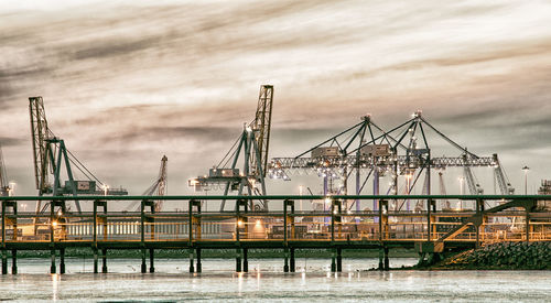 Cranes at harbor against sky