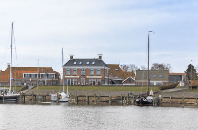 Sailboats in river by houses against sky