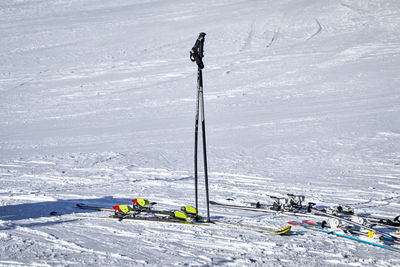 Ski poles stand upright in the white snow and some different colored skis lie next to them