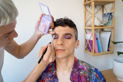 Caucasian transgender man getting makeup done by his boyfriend at home