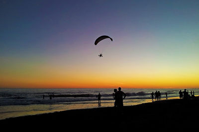 Silhouette people on beach against sky during sunset