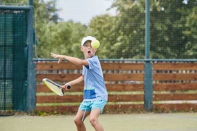 Portrait of cute boy hitting ball with racket at tennis court