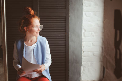 Woman with documents sitting against wall