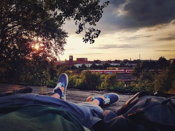 Low section of man relaxing in city against sky during sunset