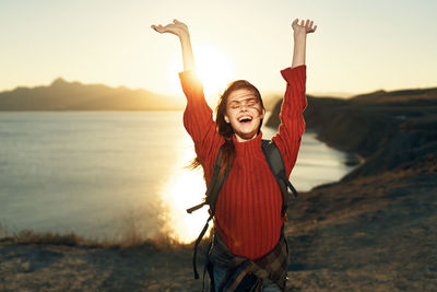 Portrait of woman with arms raised standing against sky during sunset