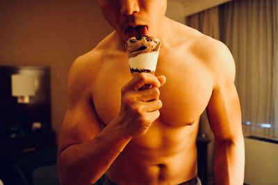 Midsection of shirtless man eating ice cream at home