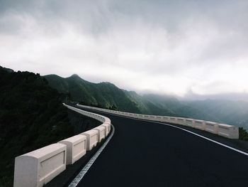 Bridge amidst mountains against sky during foggy weather