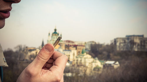 Cropped image of person holding cityscape against sky