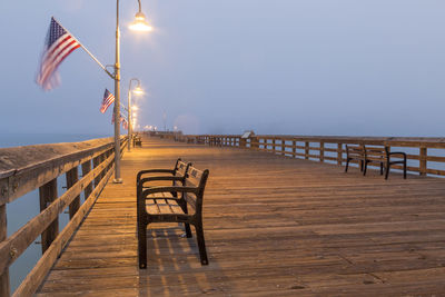 Empty chairs and table on pier against clear sky