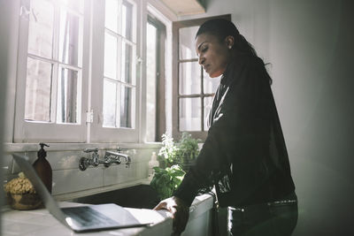 Side view of female professional looking at laptop while standing by sink at home office