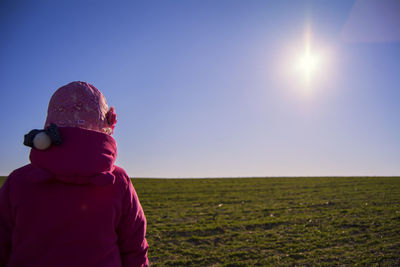 Rear view of girl in pink jacket on grassy field against sky