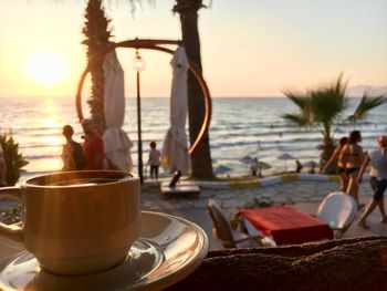 Coffee cup on table by sea against sky during sunset