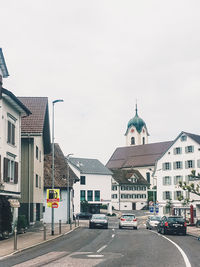 Cars on road by buildings against sky in city