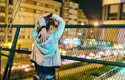 Unrecognizable young brunette woman athlete stretching her arms before run on the city at night