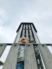 Low angle view of girl standing at railing against cloudy sky