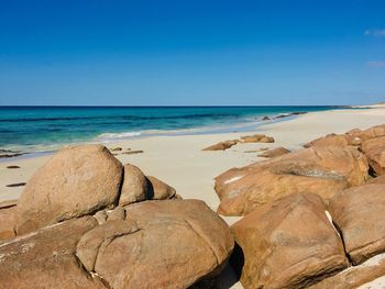 Scenic view of rocks on beach against blue sky