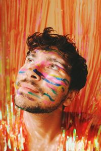 Queer young man in colorful face paint in glowing curtains at a party