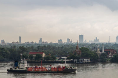 Boats in river by city against sky