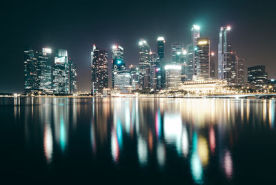 Illuminated buildings by river against sky at night