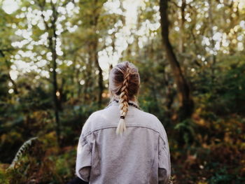 Rear view of woman with braided hair standing against trees at forest