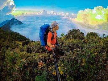 High angle view of man holding monopod while standing amidst plants on mountain