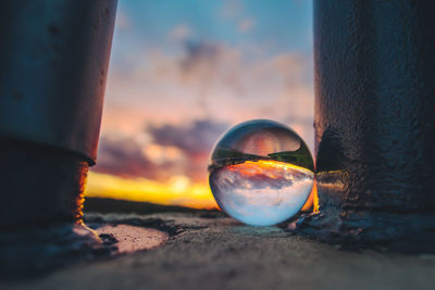 Close-up of crystal ball on beach against sky during sunset