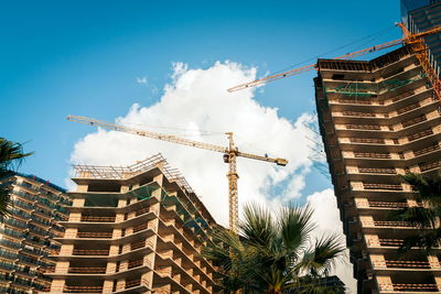 Low angle view of crane by building against sky