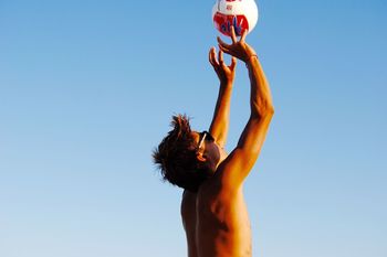 Low angle view of shirtless man playing volleyball against clear blue sky
