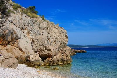 Rock formation by sea against blue sky